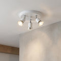 White circular ceiling plate with three adjustable spotlights illuminating a textured wall.