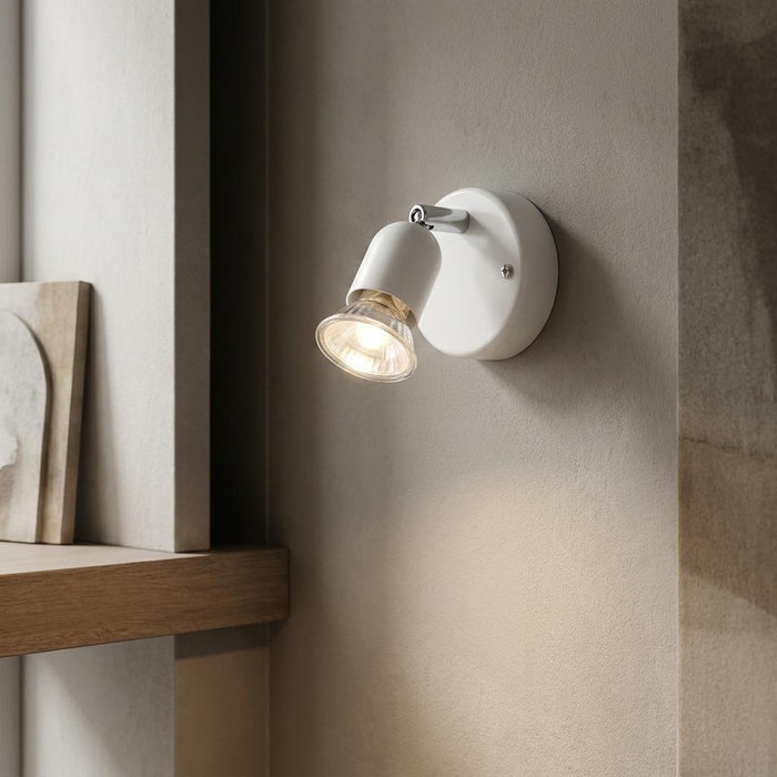 White single adjustable spotlight mounted on a wall, illuminated and casting a warm glow downwards.