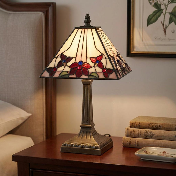 A Tiffany-style table lamp with red floral glass shade and bronze base sits on a wooden bedside table.