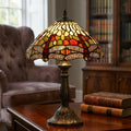 Dragonfly Tiffany table lamp with a multi-coloured stained glass shade and bronze base on a wooden table.