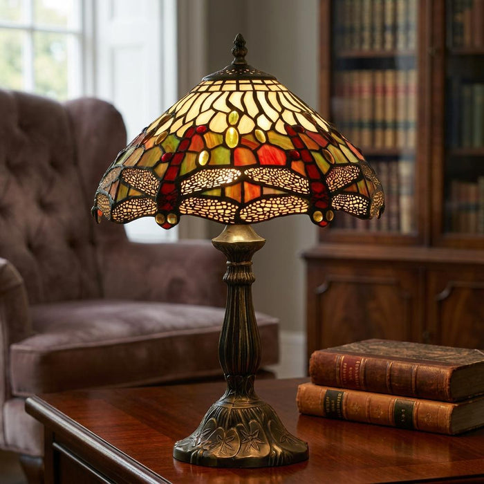 Dragonfly Tiffany table lamp with a multi-coloured stained glass shade and bronze base on a wooden table.