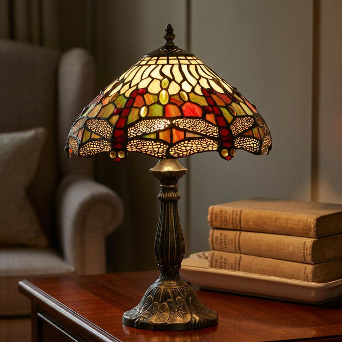 Dragonfly Tiffany table lamp with an ornate stained glass shade on a wooden table beside old books.
