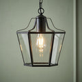 Black lantern-style pendant light with clear glass panels and an Edison bulb against a green wall.