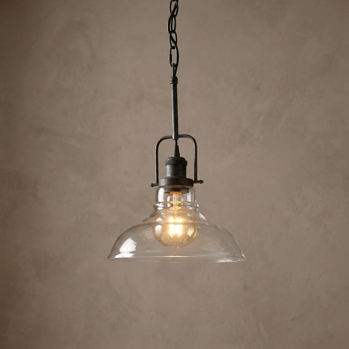 Industrial wrought iron pendant light with a clear glass dome shade and a warm glowing bulb.