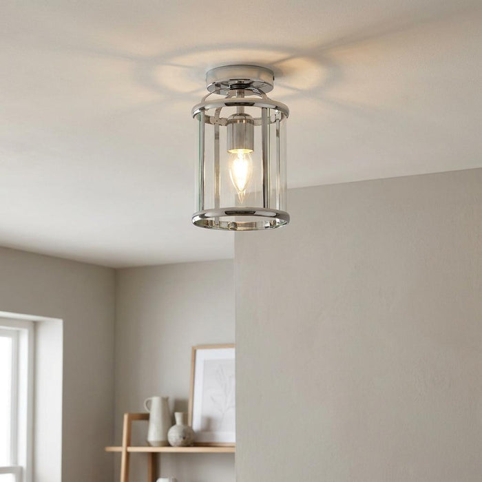 Modern chrome and glass cylindrical ceiling flush light with a lit candle bulb on a white ceiling.