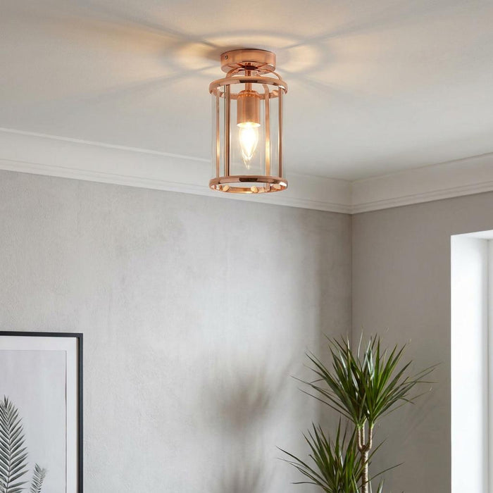 Copper ceiling flush light with a cylindrical glass shade and polished metal frame, illuminated on a plain ceiling.