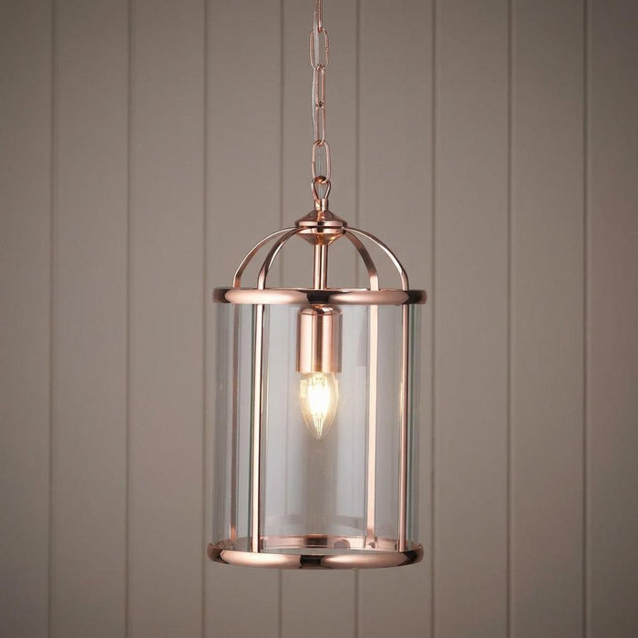 Elegant copper ceiling lantern with a clear glass cylinder and lit bulb against wood paneling.