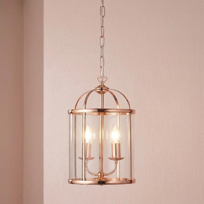 Two-light copper Fern lantern with clear glass cylinder and dome top hanging against a pink wall.