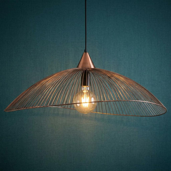 Copper wire cage pendant light with an undulating shade and exposed bulb against a teal wall.