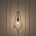 Geometric black metal and glass pendant light with a glowing bulb against a paneled wall.