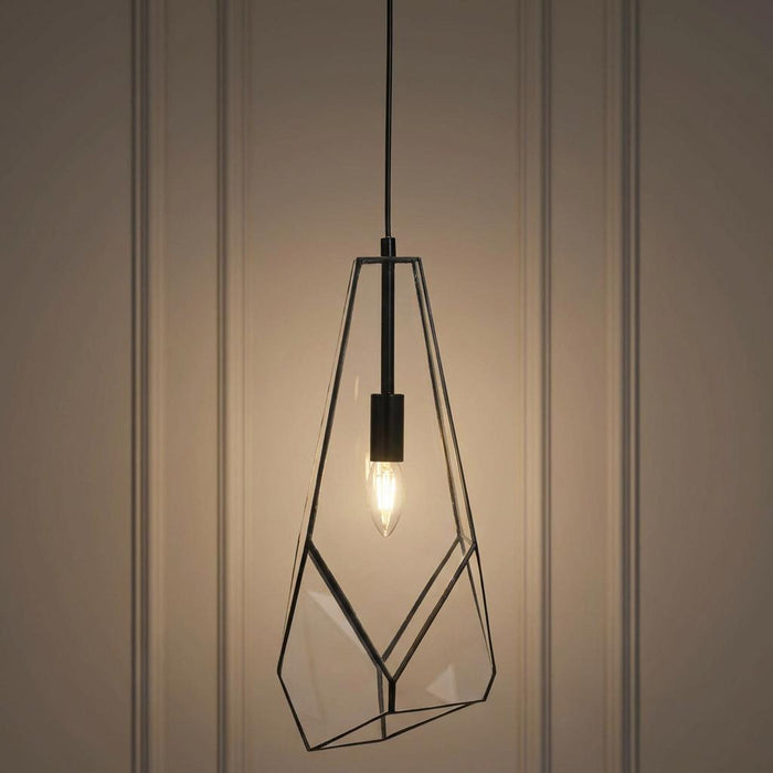 Geometric black metal and glass pendant light with a glowing bulb against a paneled wall.