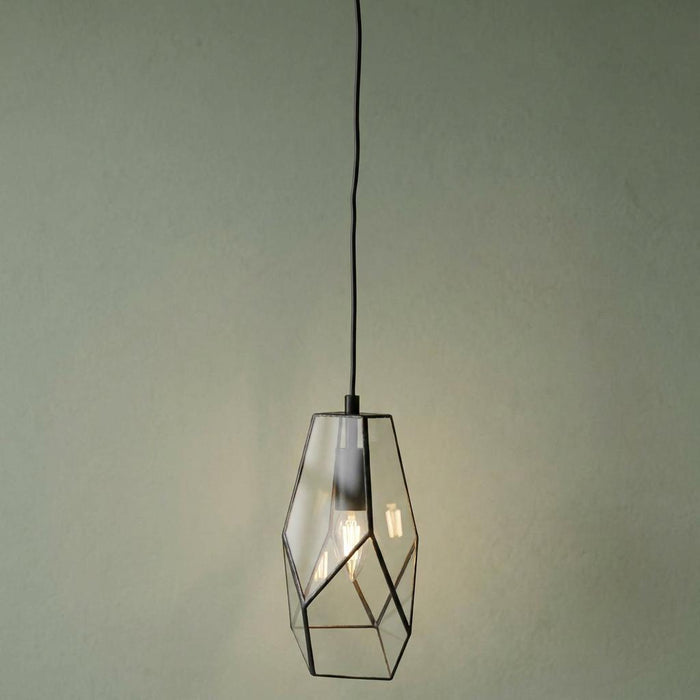 Geometric glass pendant light with a black frame hanging against a textured sage green wall.