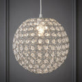Spherical chrome pendant light with acrylic crystal buttons illuminated against a grey wall.