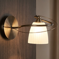Oaks Lighting Leke antique brass wall light with a glowing frosted glass shade on a dark wood wall.