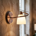 Copper wall light with a curved arm and glowing fluted glass shade mounted on a textured plaster wall.
