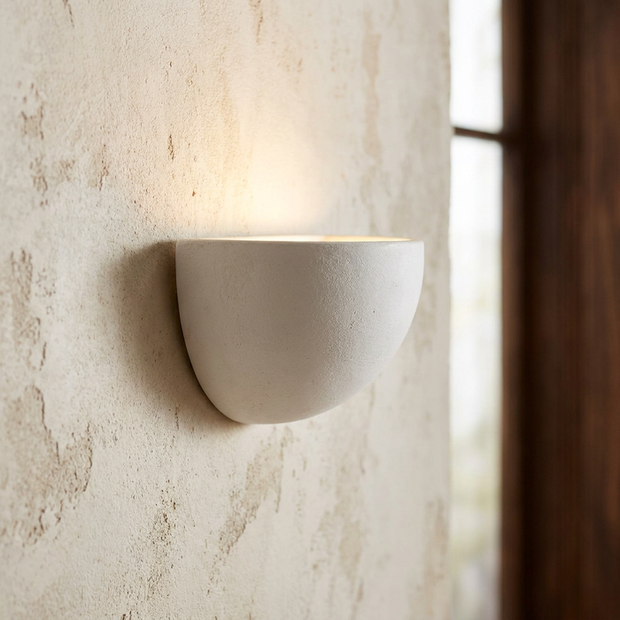 Semi-circular white ceramic wall uplighter mounted on a textured beige wall, casting a warm glow upwards.