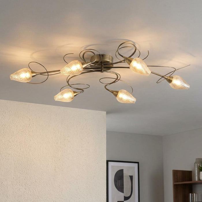 Antique brass 6-arm semi-flush ceiling light with swirling arms and textured glass shades in a modern room.
