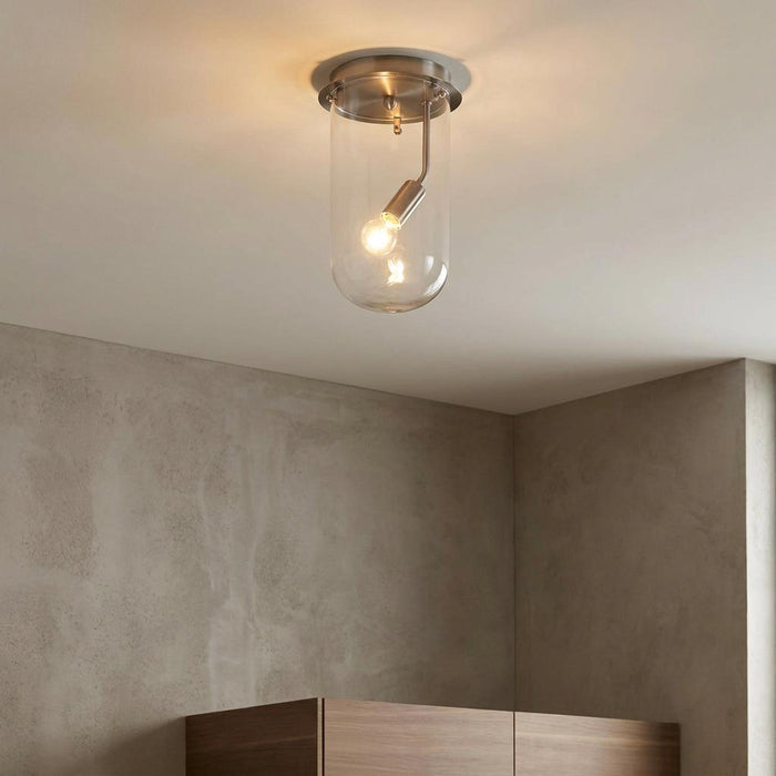 Antique chrome flush ceiling light with a clear glass cylindrical shade and a glowing bulb.