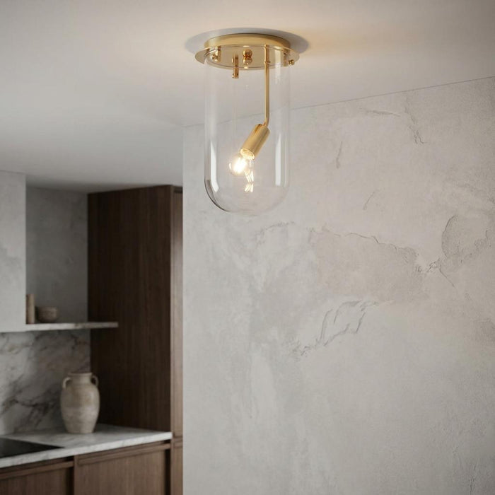 Gold flush ceiling light with a clear cylindrical glass shade in a modern kitchen setting.