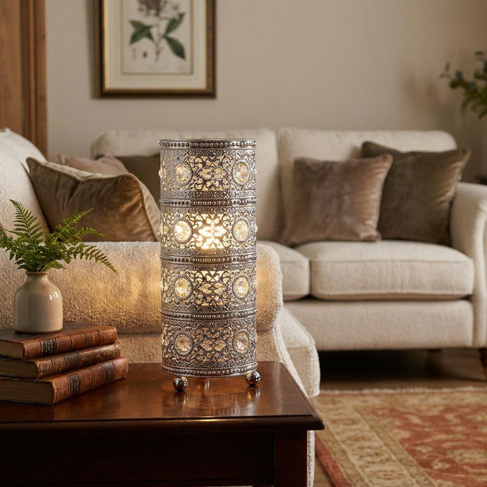 Ornate chrome cylindrical table lamp with crystal beads glowing on a wooden side table in a cozy living room.