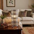 Ornate chrome cylindrical table lamp with crystal beads glowing on a wooden side table in a cozy living room.
