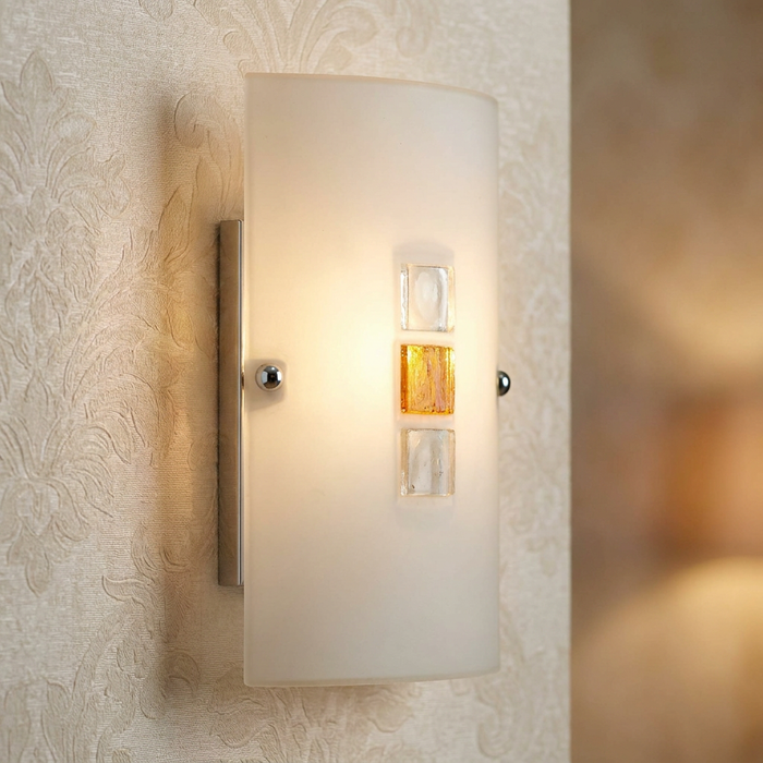 Frosted glass wall light with amber and clear glass jewel details mounted on textured cream wallpaper.