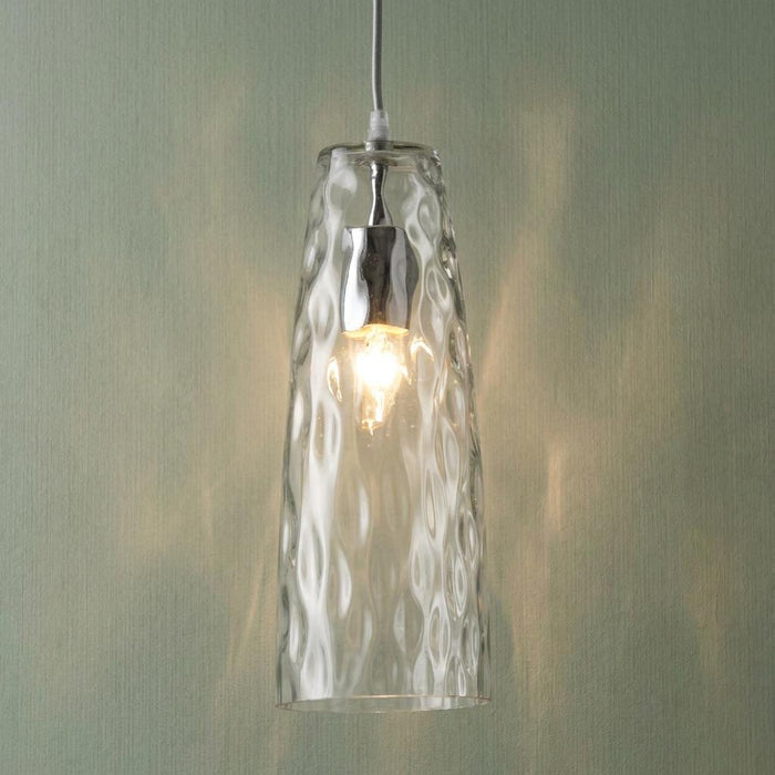 Oriata mottled glass ceiling pendant with a tall dimpled clear shade illuminated against a light green wall.