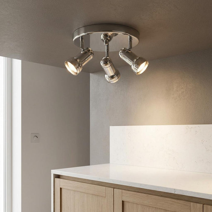Chrome three-light adjustable ceiling spotlight illuminated above a modern white countertop in a minimalist kitchen.