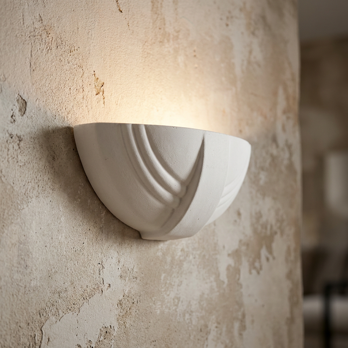 White ceramic wall light with Art Deco ridges casting a warm upwards glow on a textured plaster wall.