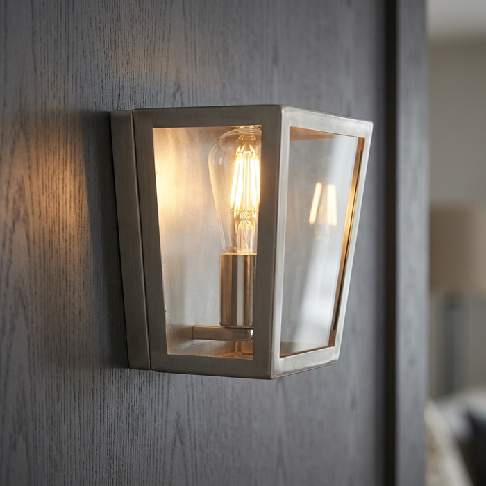 Oaks Lighting Riga antique chrome wall lantern with a glowing filament bulb on a dark wood panel.
