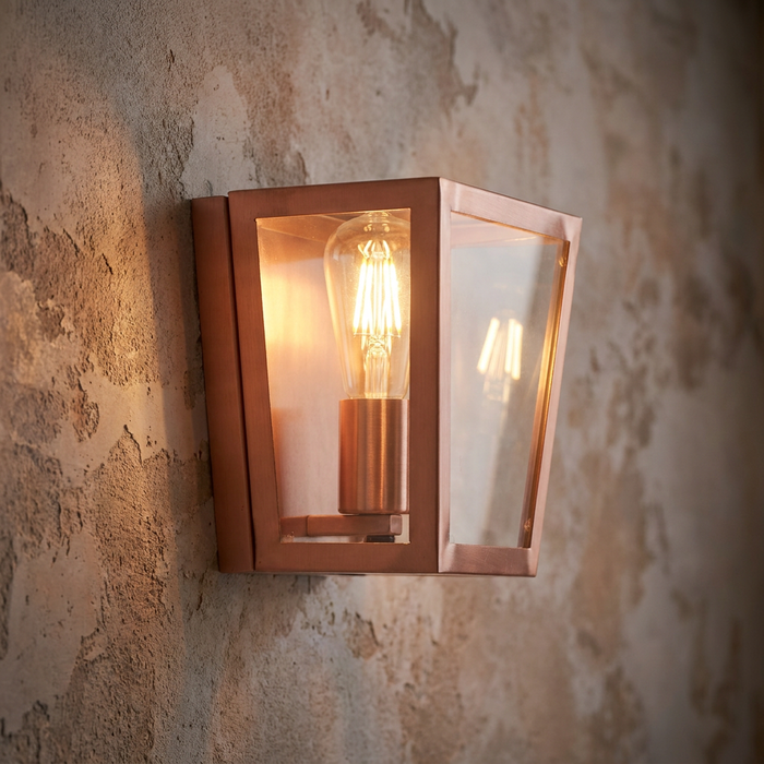 Copper lantern wall light with a glowing filament bulb mounted on a textured stone wall.