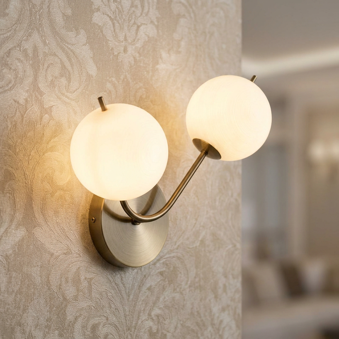 Two glowing opal glass globes on curved antique brass arms mounted against damask-patterned wallpaper.