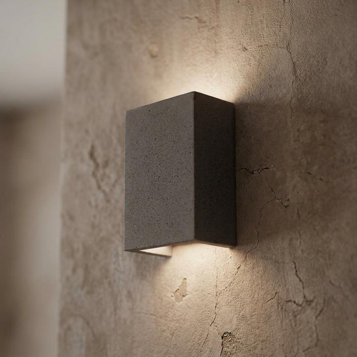 Rectangular black sandstone wall light casting a warm up-and-down glow on a textured, cracked plaster wall.