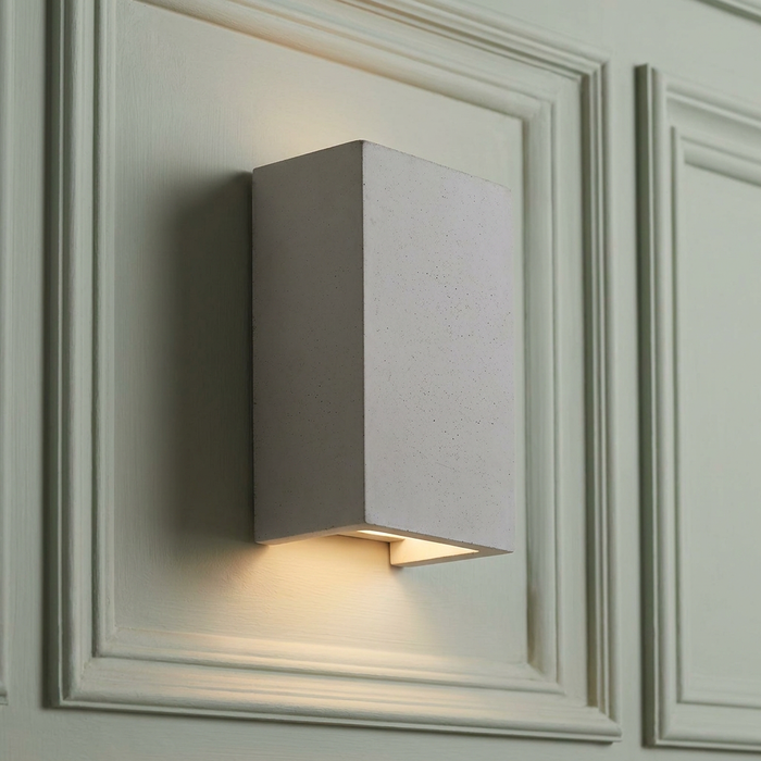 Rectangular concrete wall light emitting a warm up-and-down glow on a pale paneled wall.