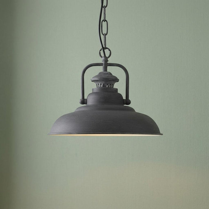 Industrial concrete grey ceiling pendant light with a wide dome shade hanging against a pale green wall.
