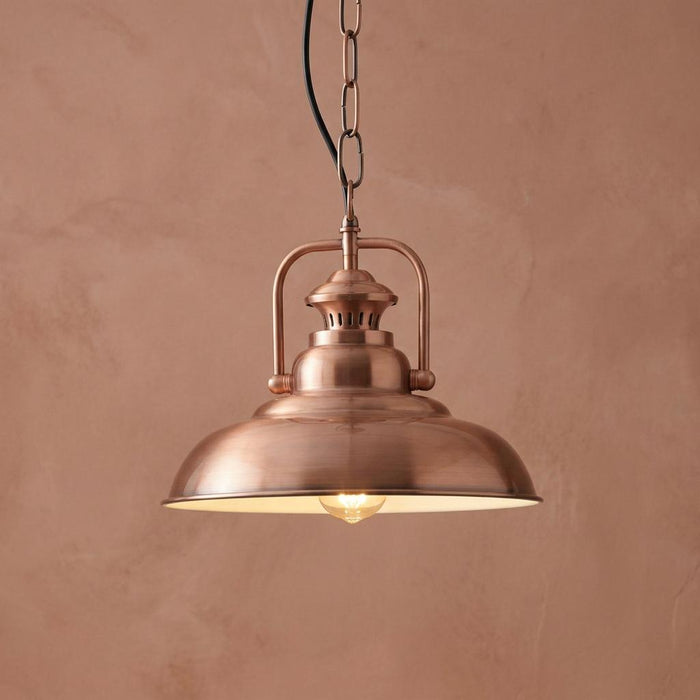Industrial copper pendant light with a domed shade hanging against a textured terracotta-colored wall.