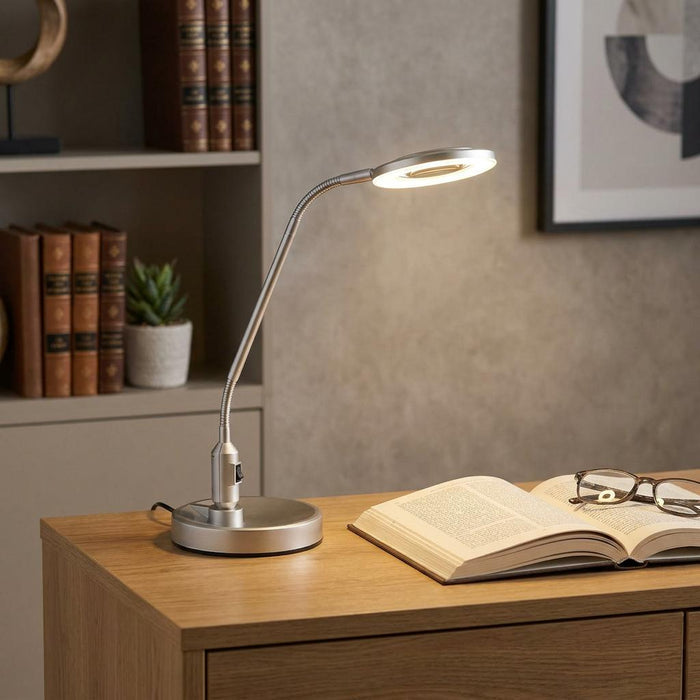 Silver LED magnifying table lamp with a flexible neck illuminating an open book on a wooden desk.