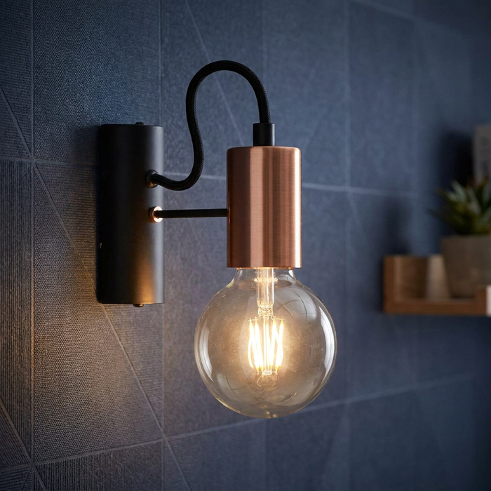 Modern black and copper wall sconce with an exposed globe bulb lit against a blue textured wall.