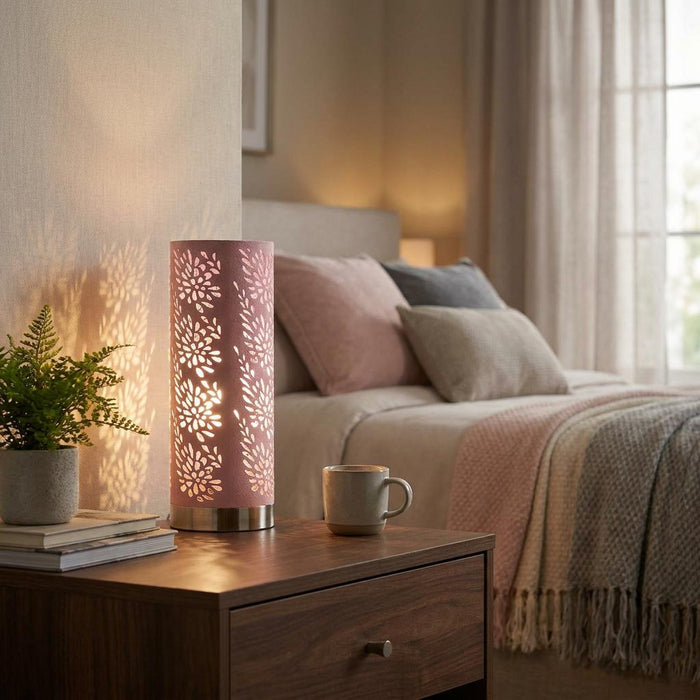 A pale pink cylindrical table lamp with floral cut-outs glows on a bedside table, casting light patterns on the wall.