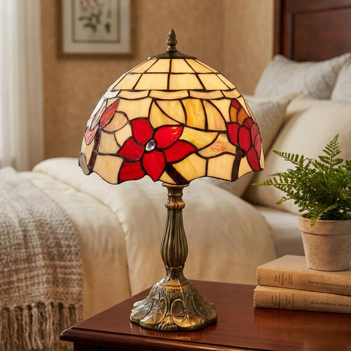 A Tiffany-style table lamp with red floral stained glass on an ornate bronze base, set on a bedroom nightstand.