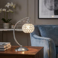 Oaks Lighting Toulon chrome table lamp with a crystal beaded sphere shade on a wooden table next to a blue armchair.
