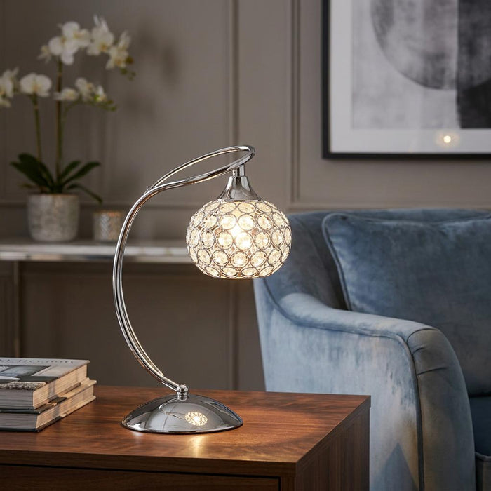 Oaks Lighting Toulon chrome table lamp with a crystal beaded sphere shade on a wooden table next to a blue armchair.