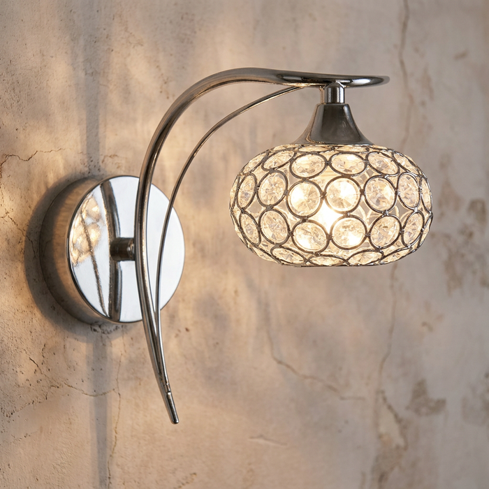Polished chrome wall light with a curved arm and glowing crystal lattice shade on a textured wall.