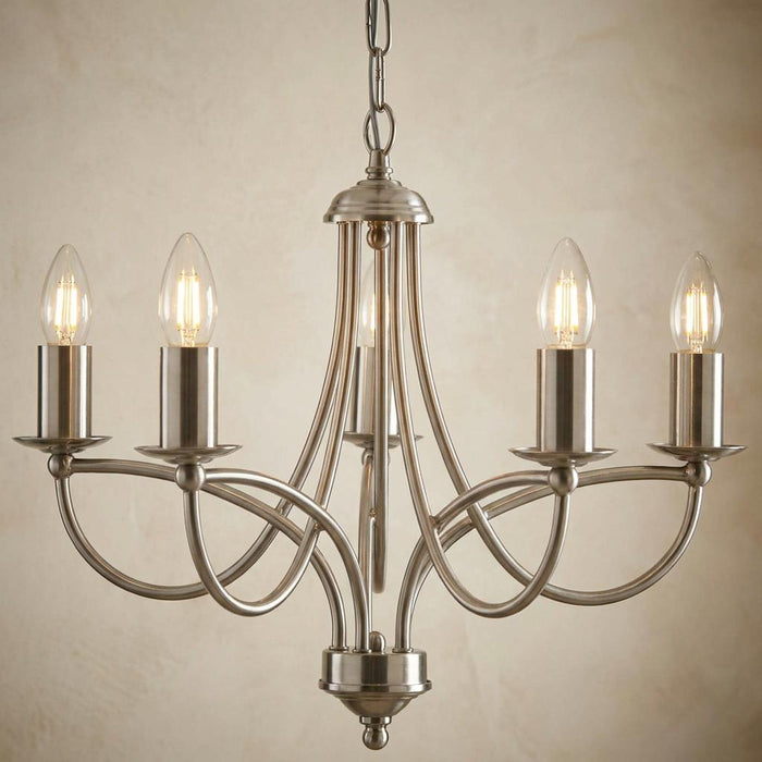 Oaks Loop Antique Chrome 5 Light Chandelier with looped arms and candle-style bulbs against a textured wall.