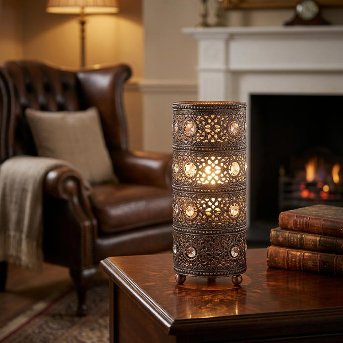 Antique copper lattice lamp with crystals on a wooden table in a cozy living room with a fireplace.
