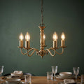 Five-light antique brass chandelier with glowing candle bulbs hanging above a set dining table with a green wall.