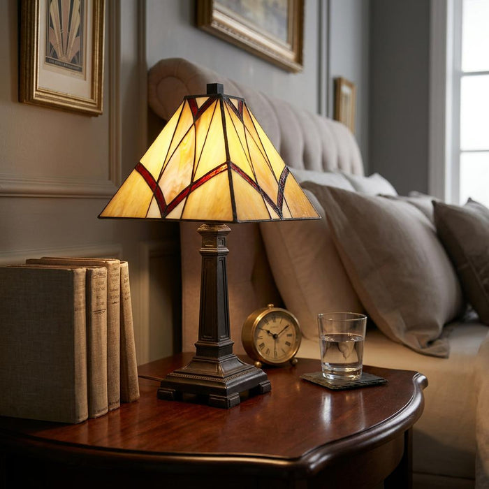 Small Oaks Portia Tiffany lamp with geometric stained glass on a wooden nightstand in a cozy bedroom setting.