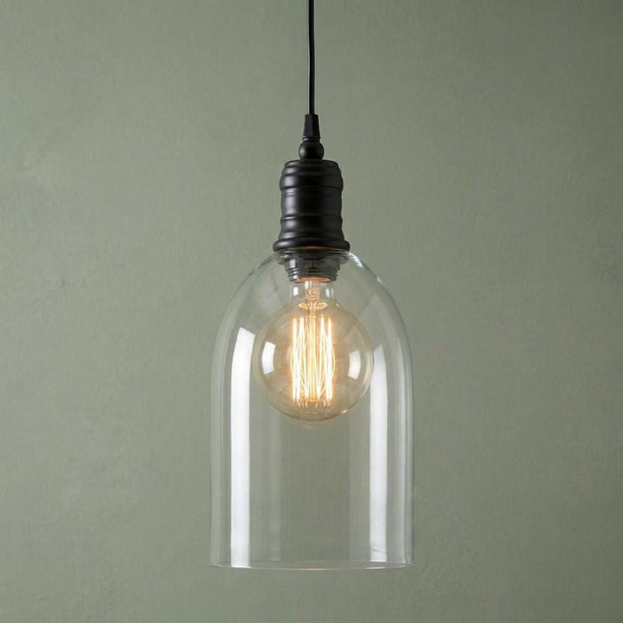 Oaks Randers pendant light featuring a clear glass dome shade and glowing filament bulb on a green wall.