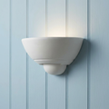 White bowl-shaped ceramic wall sconce glowing against a light blue vertical wood plank wall.