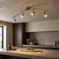 Antique brass curved 4-light spotlight fixture illuminating a modern kitchen island and cutting board.